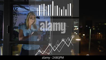 Image of data processing over caucasian woman using tablet while working late at office Stock Photo