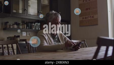 Image of envelope icons in circles over senior biracial woman scrolling on smartphone at home Stock Photo