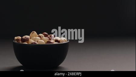 roasted hazelnuts in black bowl on black background, wide photo Stock Photo
