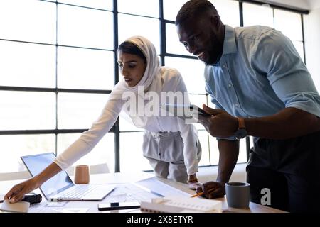 At modern office, diverse team working together, reviewing architect drawings. African American male colleague holding tablet, Indian female team lead Stock Photo