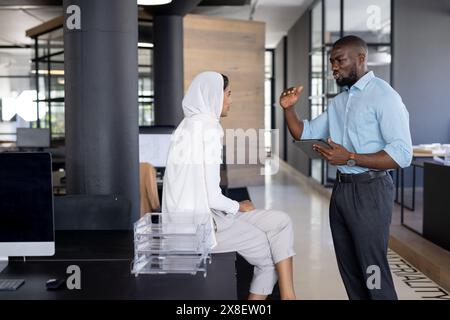 In modern office, diverse team with African American and indian colleagues talking. African American male with short hair and beard holding tablet, in Stock Photo