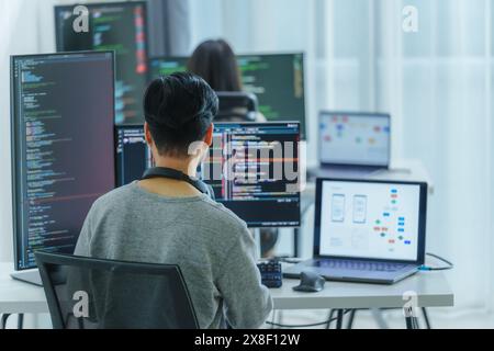 Asian software developers working on multiple screens displaying code and application diagrams in a modern office Stock Photo