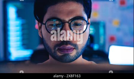 Close-up of a programmer intensely focused on his work, with computer code reflecting in his glasses. Stock Photo