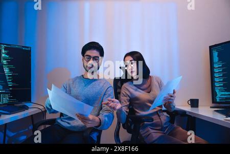 Asian software developers teams working on multiple screens displaying code and application diagrams at night in modern office Stock Photo