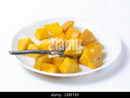 Natural ripe delicious sliced mangoes on white background served ready to eat with spoon on white plate. Stock Photo