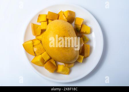 Ripe mango with sliced mango around it on white plate isolated on white background. Closeup Stock Photo