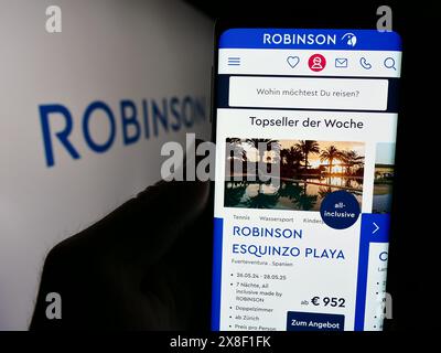 Person holding cellphone with website of German hospitality company Robinson Club GmbH in front of logo. Focus on center of phone display. Stock Photo