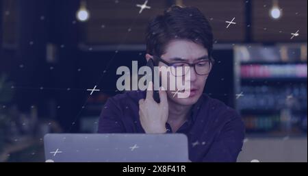 Asian father, doubling as chef, chatting on smartphone, typing on laptop Stock Photo