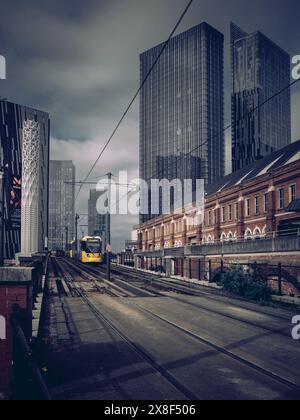 A Bee Network tram in Manchester against the backdrop of Deansgate Square tower skyscrapers with dark cloudy sky, UK weather conditions and forecast Stock Photo