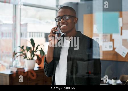 Businessman, black man and phone in office for communication with negotiation proposal for networking. Smile, African employee and talking on mobile Stock Photo