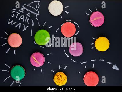 A mesmerizing painting of multi-colored macaroons resembling organisms, with colored petals on a black surface, creating a beautiful pattern that comb Stock Photo