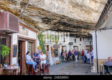 Restaurants and cafes crowd along the Calle Cuevas de la Sombra under the rock ledge overhang in the unique pueblos blanco of Setenil de las Bodegas, Spain. Residents of the tiny village of Setenil have lived in cave houses since neolithic times. Stock Photo