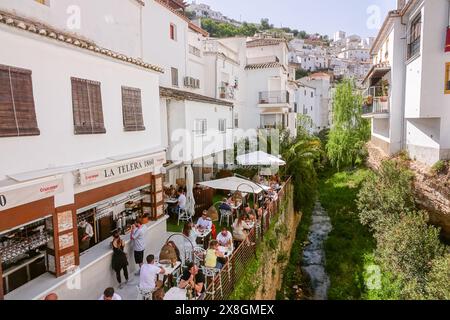 Restaurants and cafes crowd along the Calle Cuevas de la Sombra on the Trejo River n the unique pueblos blanco of Setenil de las Bodegas, Spain. Residents of the tiny village of Setenil have lived in cave houses since neolithic times. Stock Photo