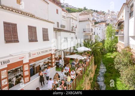 Restaurants and cafes crowd along the Calle Cuevas de la Sombra on the Trejo River n the unique pueblos blanco of Setenil de las Bodegas, Spain. Residents of the tiny village of Setenil have lived in cave houses since neolithic times. Stock Photo