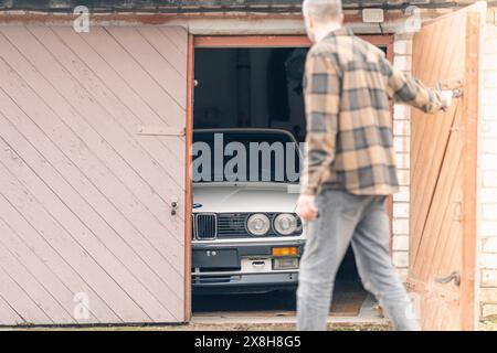 Riga, Latvia - April 1, 2024: A car owner looking on his white classic convertible BMW E30 car in the half opened garage. Stock Photo