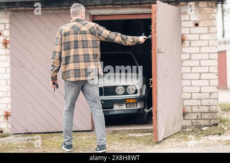 Riga, Latvia - April 1, 2024: A car owner looking on his white classic convertible BMW E30 car in the half opened garage. Stock Photo