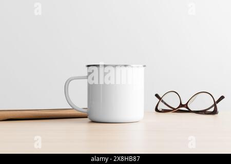 Enamel mug mockup with workspace accessories on the wooden table. Stock Photo