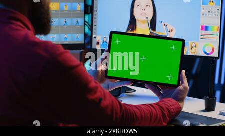 Photo editor uses green screen tablet to watch online podcast while looking at pictures taken with professional camera. Freelancer in home studio browsing images and looking at videos on mockup device Stock Photo