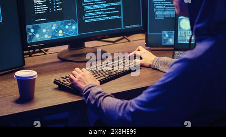Young hacker drinking coffee while running spyware software designed to gather information from users computers without their knowledge. Script kiddie doing illegal stuff in graffiti painted hideout Stock Photo