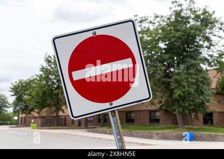 Red and white No Entry sign - school building and green trees - cloudy sky backdrop. Taken in Toronto, Canada. Stock Photo