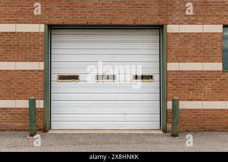 Closed white garage door set into red brick wall - patterned with lighter bricks - green bollards and concrete ground. Taken in Toronto, Canada. Stock Photo