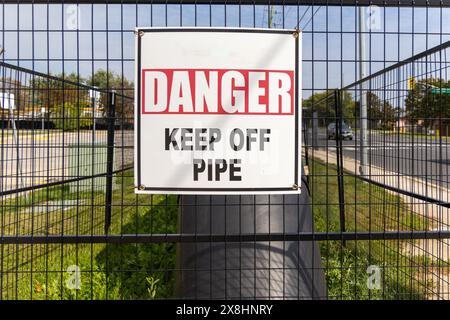 White rectangular warning sign - bold red letters stating DANGER KEEP OFF PIPE - attached to black metal fence - lush green grass and clear street vie Stock Photo