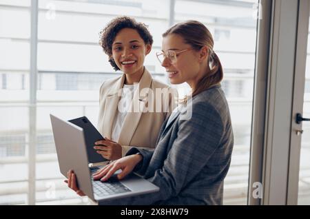 Group of female managers standing in modern office while working on laptop and digital tablet Stock Photo