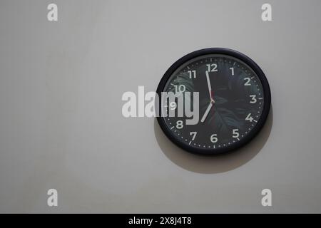 A wall clock with a picture of a leaf showing almost 7 o'clock on a white background Stock Photo