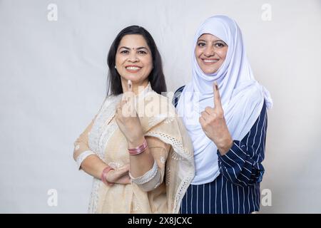 Election in india. Portrait of happy hindu and muslim women show fingers marked with ink after casting vote standing isolated over white background, P Stock Photo