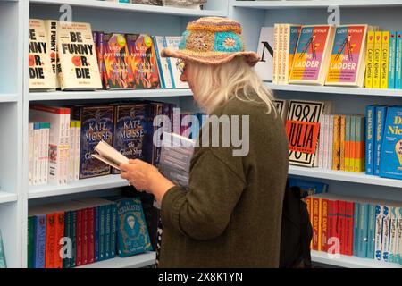 Person older woman straw hat reader reading looking at books for sale on book shelves in bookshop at the Hay Festival 2024 Hay-on-Wye UK KATHY DEWITT Stock Photo