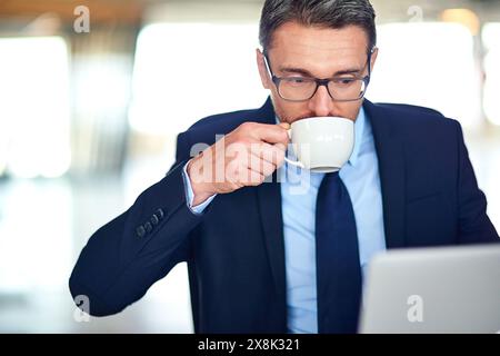 Businessman, laptop and drinking coffee with online research with morning email, project planning or office. Male person, networking and tech Stock Photo