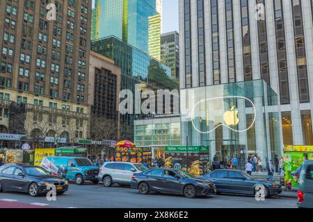 View of Fifth Avenue with car traffic, featuring the flagship Apple store and the Dior boutique located on the opposite side of the road. New York. Stock Photo