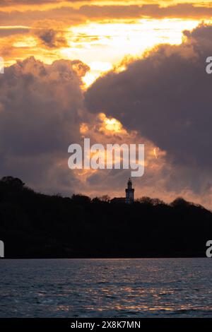 fiery sunset behind the lighthouse, sky with clouds illuminated by the sun over a lighthouse on the coast of northern Spain, orange and dark colors of Stock Photo