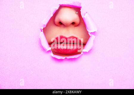 A woman's nose and mouth are visible through pink torn paper Stock Photo