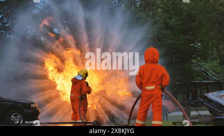 Firefighter fighting with flame using fire hose chemical water foam spray engine. Fireman wear hard hat, body safe suit uniform for protection. Rescue Stock Photo