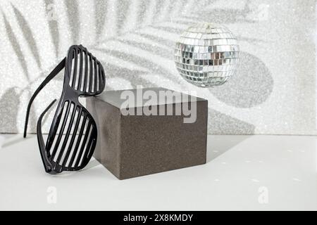 Gray backdrop with cube , party grate shades, disco mirror ball and palm leaf shadows on a silver glitter wall. Empty stage on grey background for pro Stock Photo