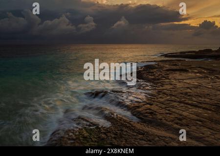 A breathtaking seascape of turquoise waters, white sand and jagged rocks set against a vibrant tropical sky and wispy clouds. Stock Photo