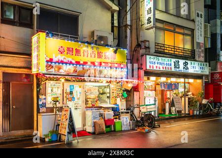 Chinese restaurant and Japanese Izakaya, (bar with food), next to each other in Otsuka, Tokyo. Night time with diners illuminated. Stock Photo