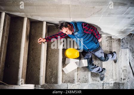 Male worker lying on the stairs after fall. Work injury, accident in workplace. Stock Photo