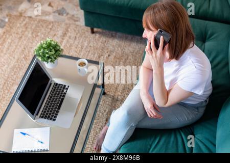 Freelancer working at home with laptop and mobile. Boring woman surfing net and talking on phone,  copy space Stock Photo
