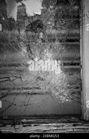 Close-up of a shattered window pane with cracked glass, highlighting textures and decay in monochrome. Stock Photo