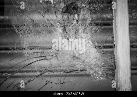 Close-up of shattered glass window capturing the intricate web of cracks and central impact point in black and white. Stock Photo