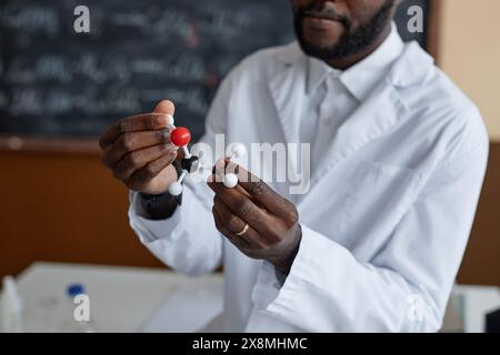 Crop shot of young Black teacher wearing white lab coat holding chemical structure model in hands while explaining subject during lesson Stock Photo