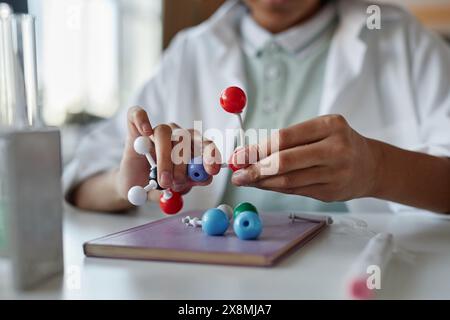 Closeup of hands of unrecognizable Black schoolboy wearing white lab coat sitting at desk assembling molecular structure model Stock Photo