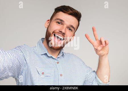 Young millennial man showing V - sign and making selfie Stock Photo