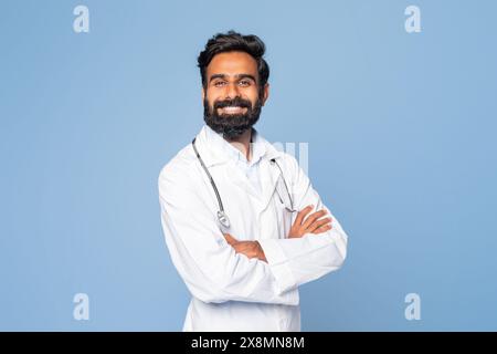 Cheerful Indian Doctor Standing With Crossed Arms Against Blue Background Stock Photo
