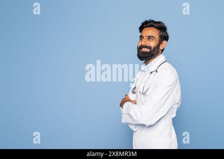 Doctor in White Coat Smiling While Standing Against Blue Background Stock Photo