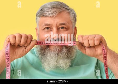 Overweight happy mature man with measuring tape on yellow background. Weight loss concept Stock Photo