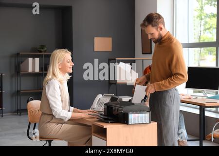 Mature businesswoman with her male colleague printing document in office Stock Photo