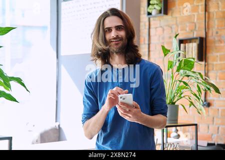 Young 30s stylish bearded man with long hair using smartphone Stock Photo